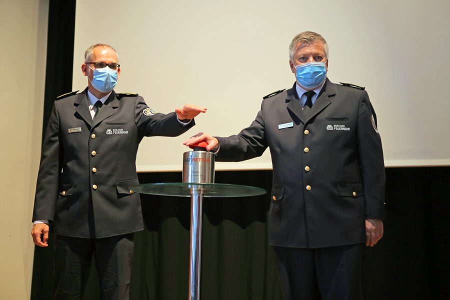 Zwei Männer in Uniform drücken auf roten Knopf