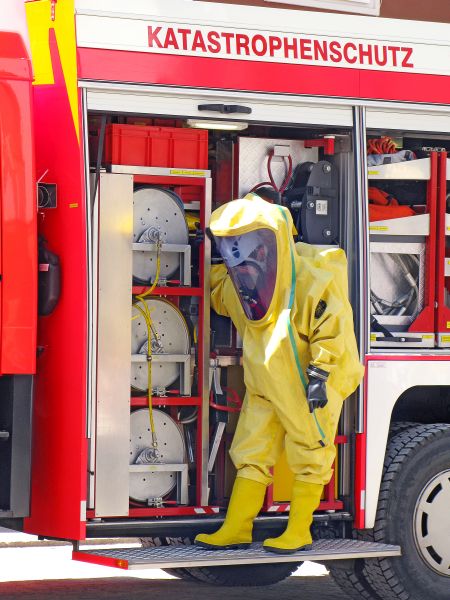 Ein Mensch im Schutzkostüm gegen chemische Gefahrstoffe vor dem Spezialauto Katastrofenschutz