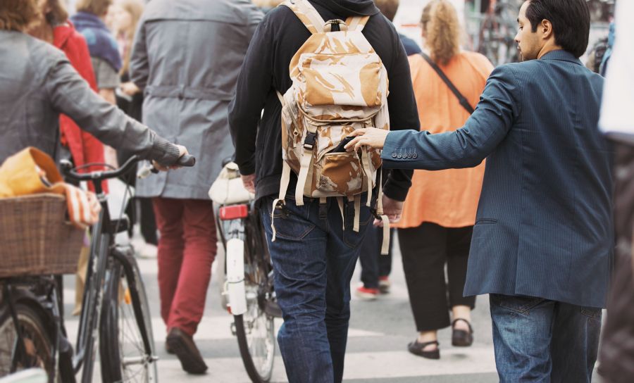 Ein Man klaut heimlich Geld aus dem Rücksack bei einem Passanten